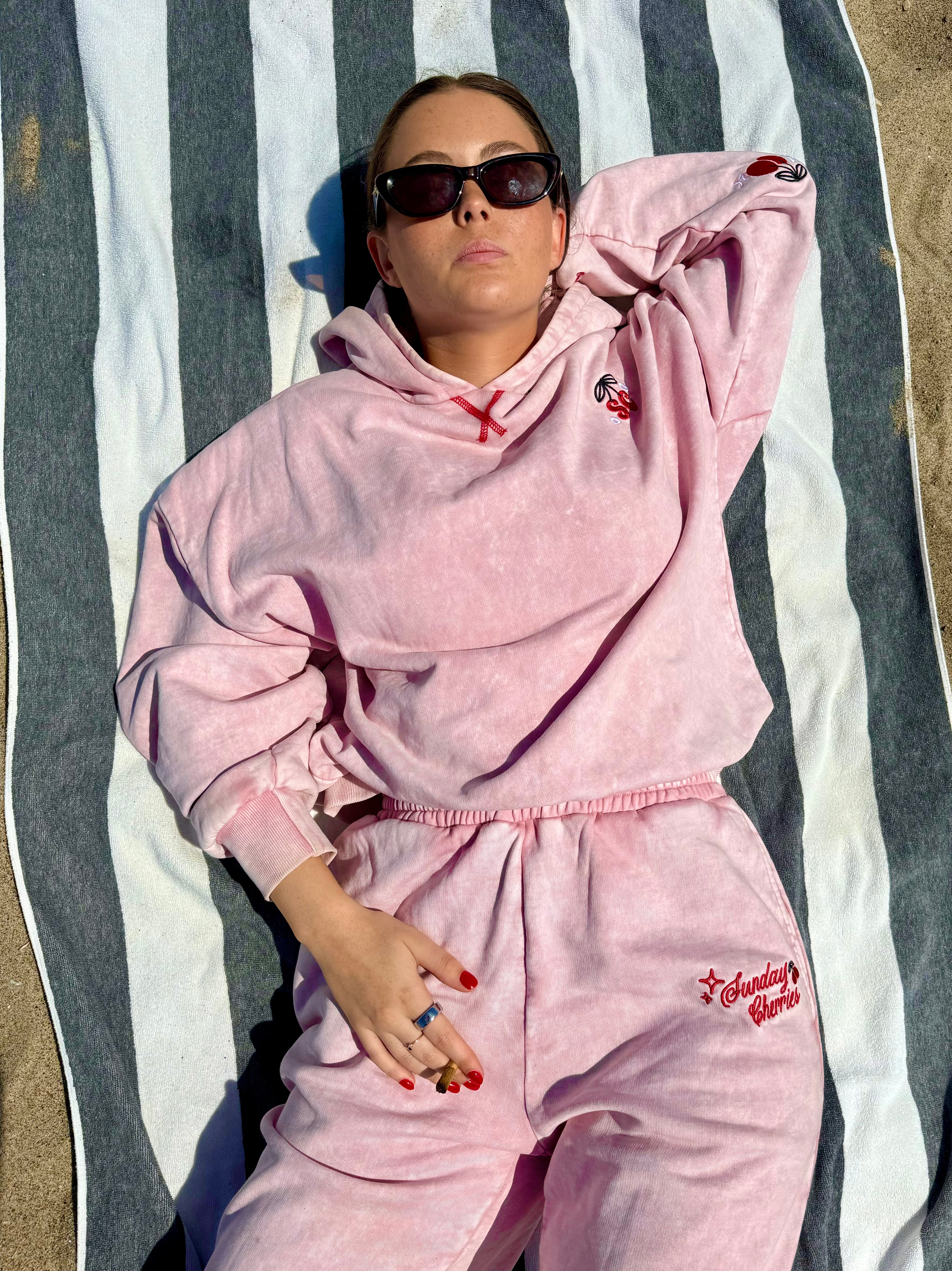 Lexi in Sunday Cherries Vintage Pink Hoodie and Sweatpants on beach blanket